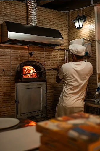 Pizzaiolo a trabalhar no forno a lenha de tijolo, com o lume aceso