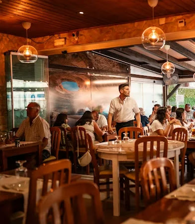Interior do restaurante: paredes de pedra, vigas de madeira e candeeiros suspensos
